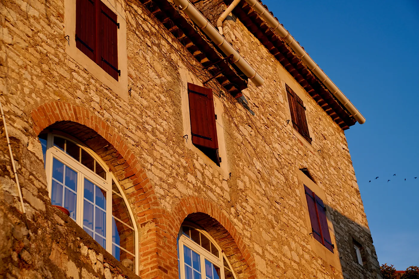 The side of a building painted by the gentle rays of the setting sun. It is common to walk by buildings with open shutters like these and hear the clinking of glasses, the laughter of couples, and the conversation of families at the dinner table.