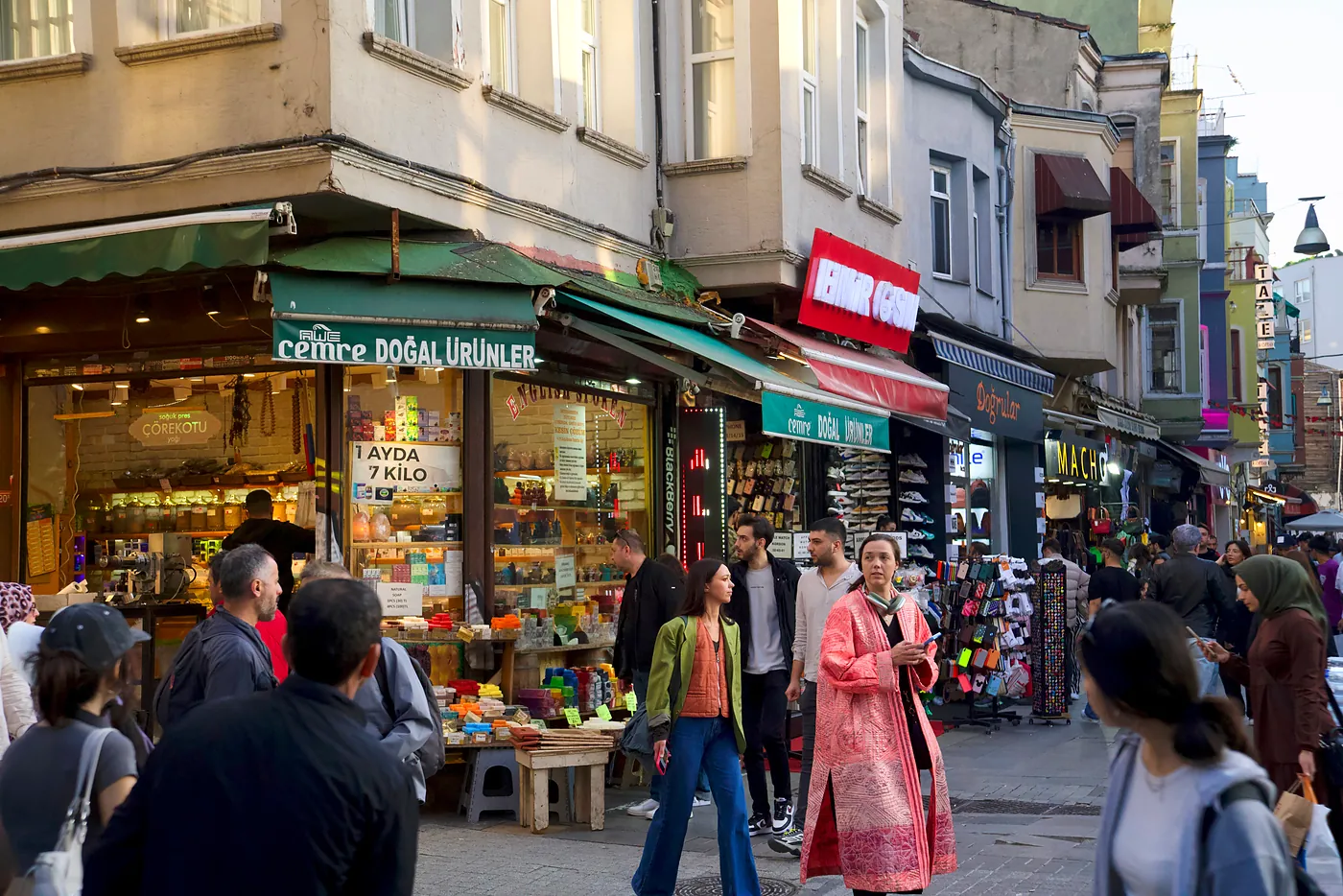 A young woman in a robe walking with her friend through a street filled with shops.