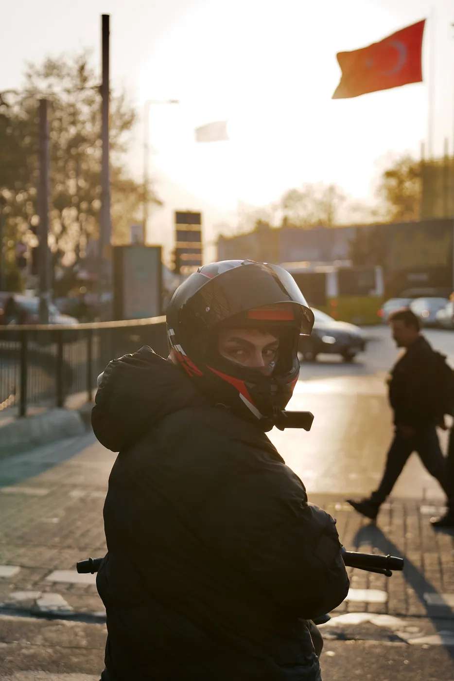 A motorcyclist looking at a honking car behind him at sunset.