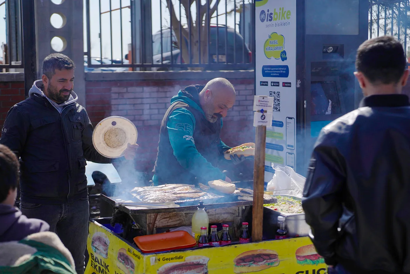 A man grilling fresh fish and making sandwhiches with his friend.