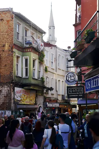 A crowded shopping street with a minaret rising above the shopfronts, Istanbul