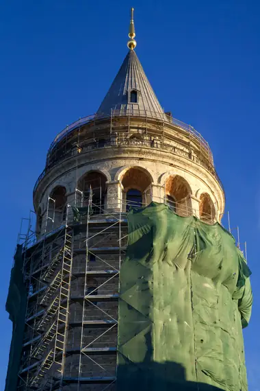 Galata Tower wrapped in scaffolding against a bright blue sky, Istanbul