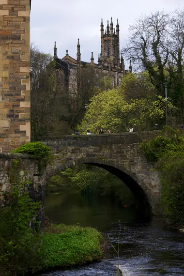 Stone bridge over the Water of Leith with a church tower rising behind the trees, Edinburgh